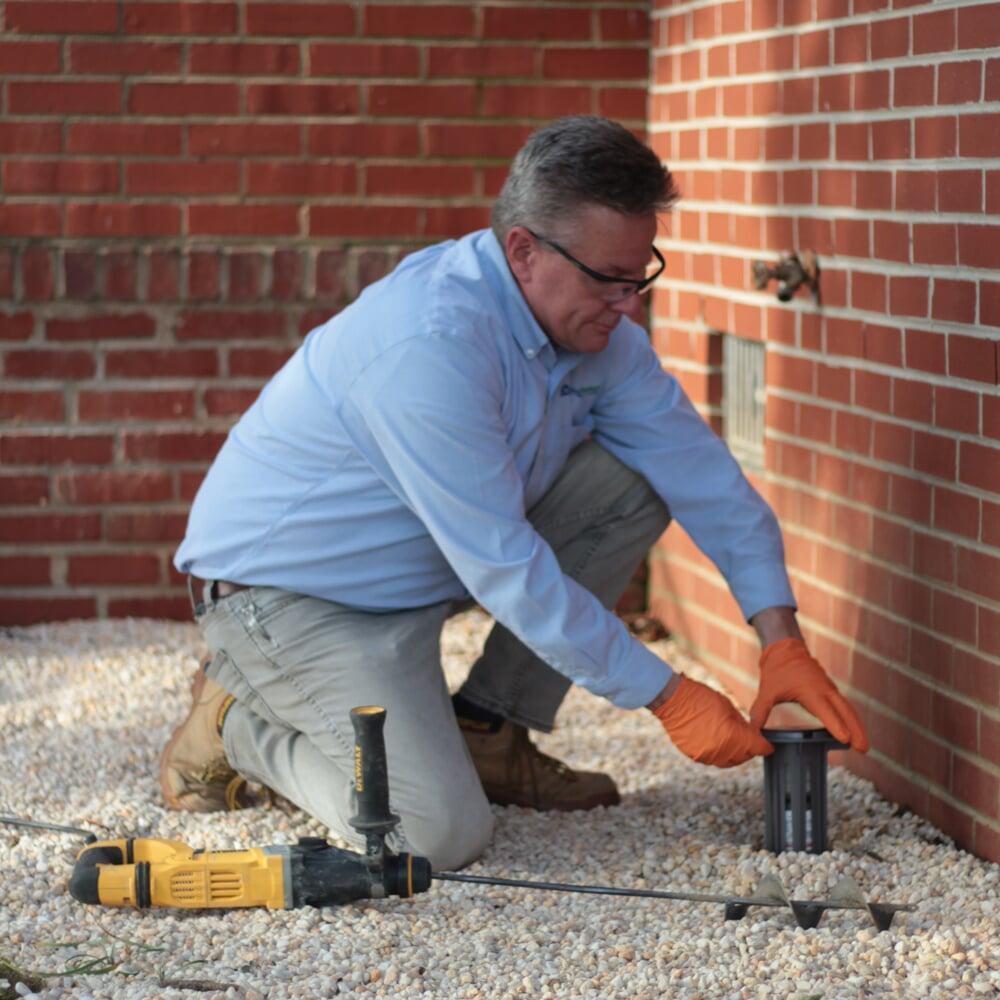Technician installing a Trelona bait station to protect a home from termite infestation.